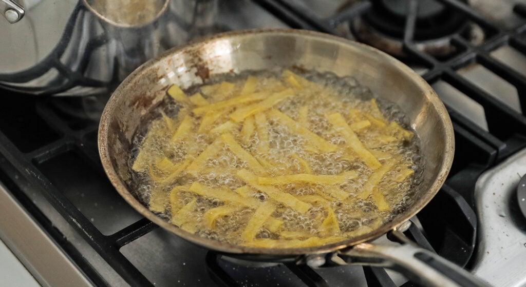 frying tortillas in oil in a pan