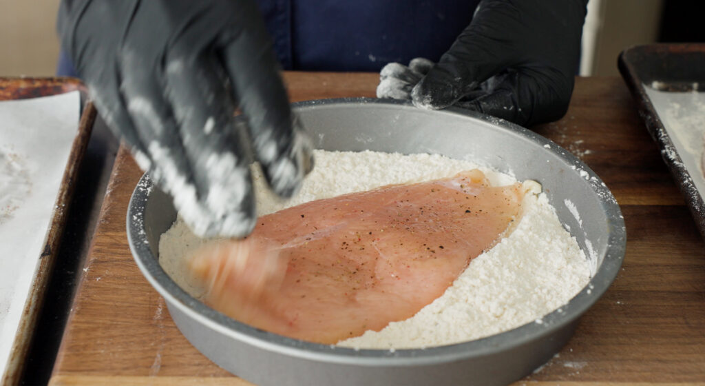Coating a chicken breast in flour in a shallow round cake pan
