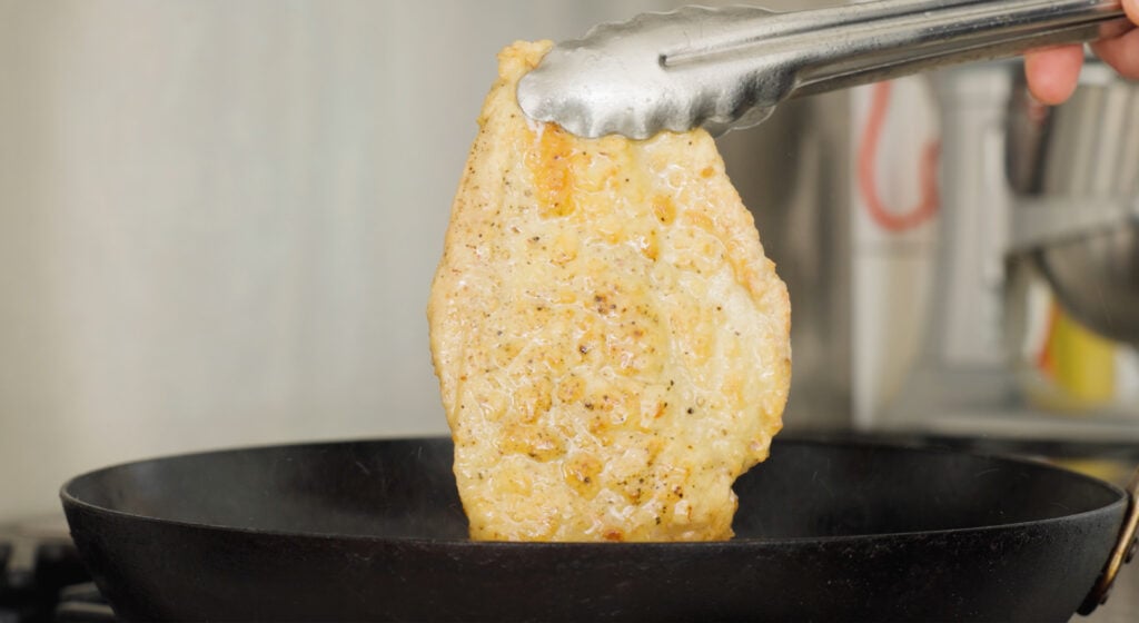 Tongs holding a browned chicken breast