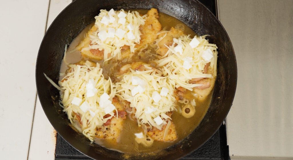 Chicken breasts in a black pan with sauce and topped with cheese