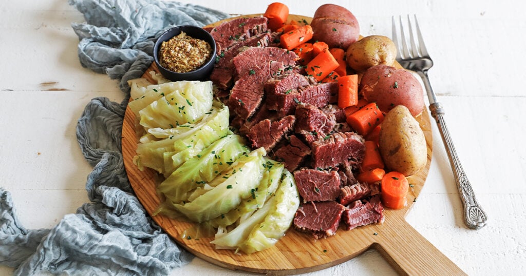 bread board full of cooked potatoes, carrots, cabbage, and corned beef
