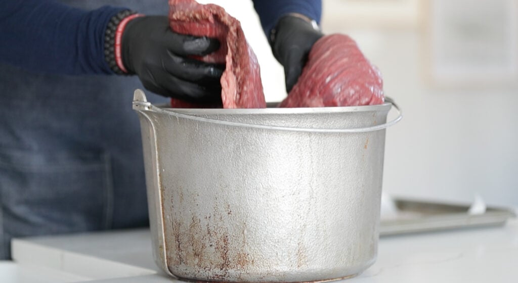 adding a raw brisket to a pot of cooled brine