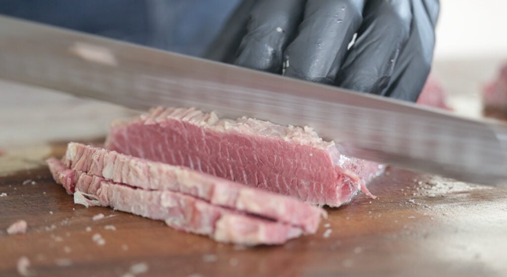 slicing cooked corned beef on a cutting board