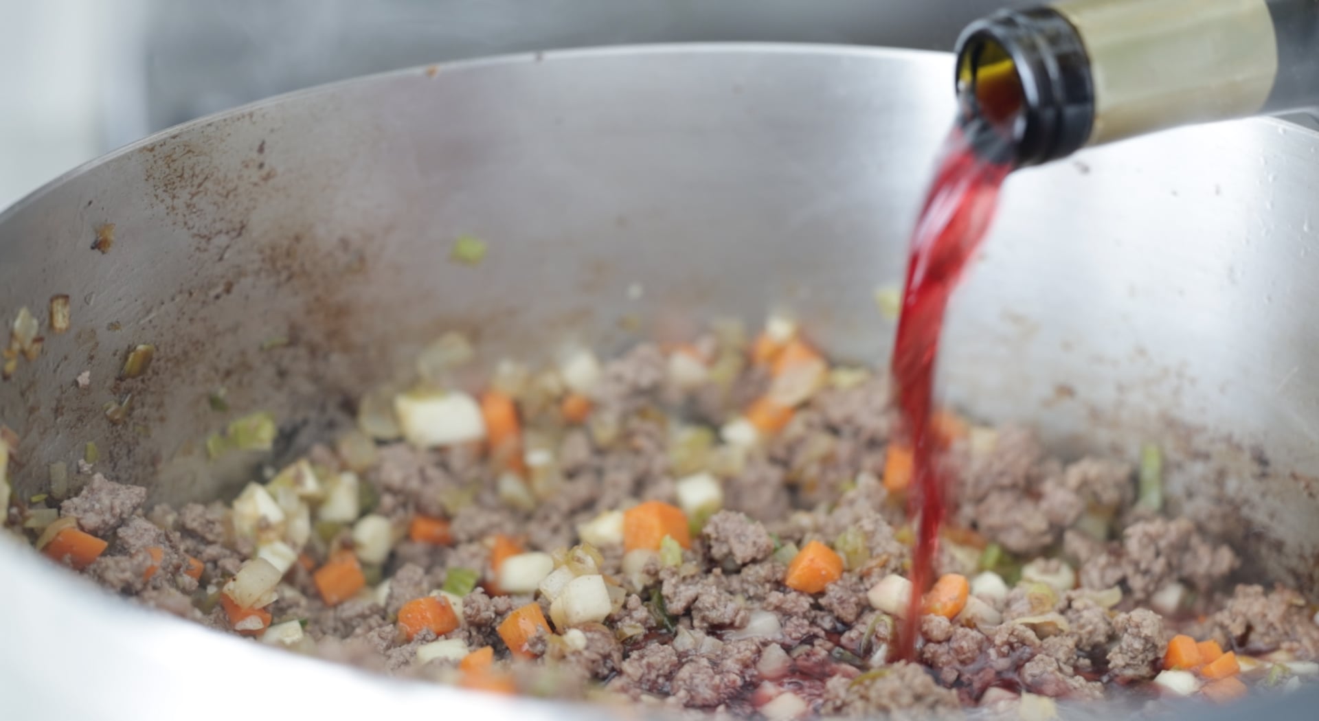 adding wine to a pot with beef and vegetables