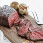London broil with serving fork and roasted garlic on a wooden board