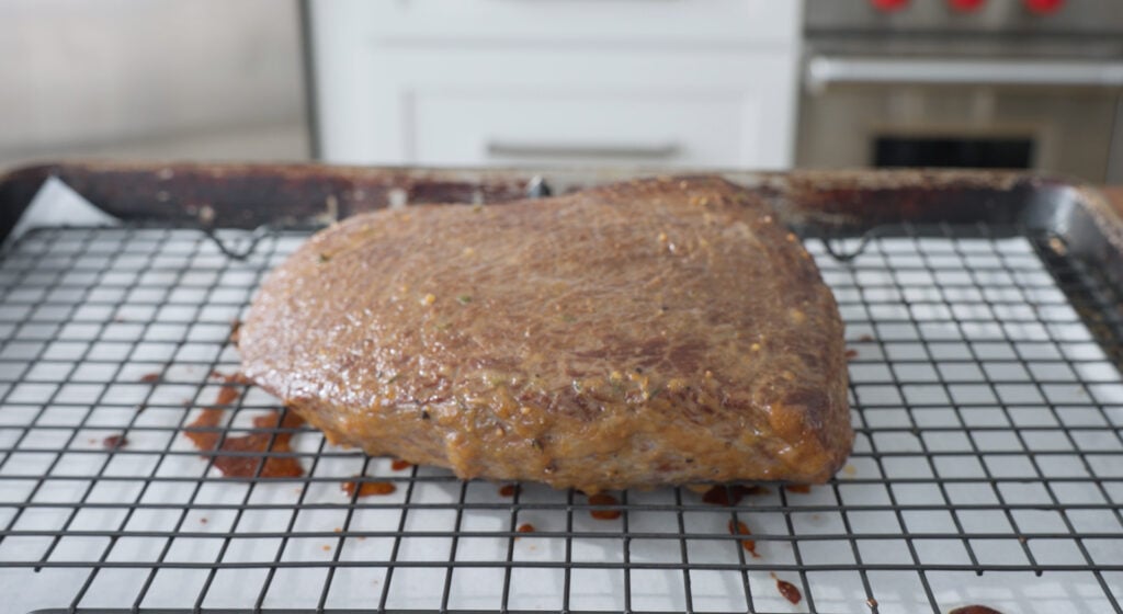 Piece of beef resting on a rack over a sheet tray