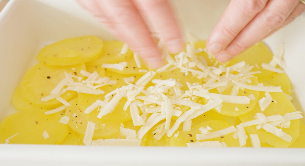 Potatoes in a dish being topped with cheese