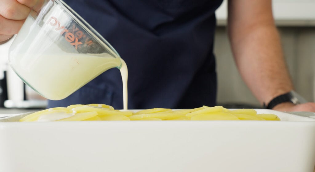 Pouring cream over the potatoes in a dish