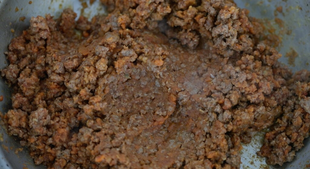 mixing tomato paste with cooked ground lamb and mirepoix