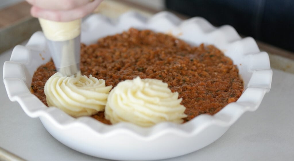 adding mashed potatoes to the top of shepherd's pie stuffing