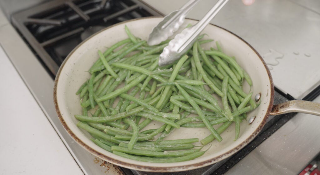 Tongs stirring Green beans in a pan