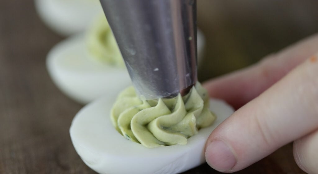 piping avocado deviled egg filling into hard boiled eggs