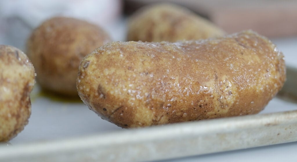 sheet tray of baking potatoes going into the oven
