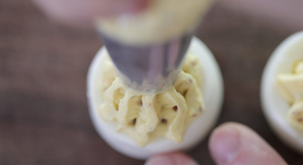 piping deviled egg filling with bacon into a hard boiled egg