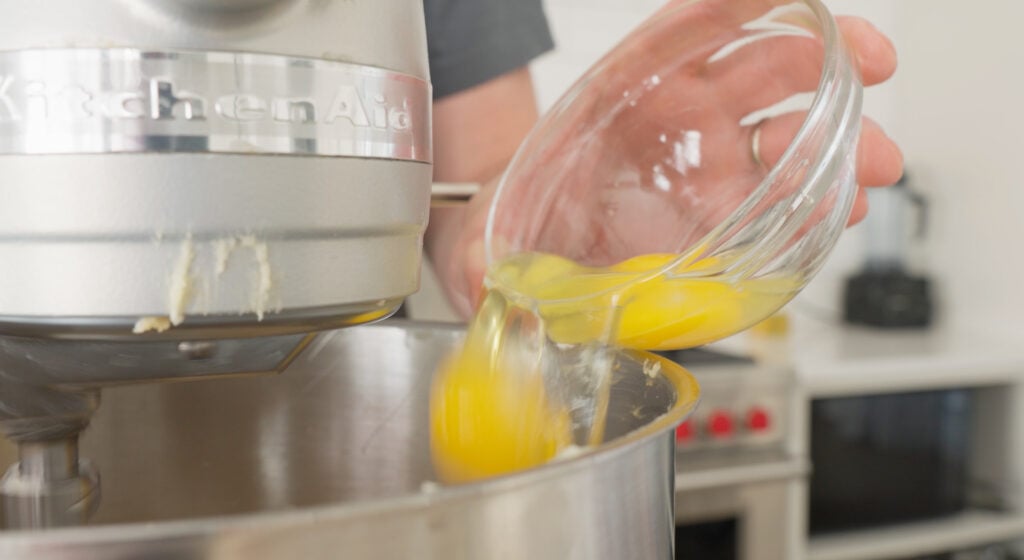 Pouring an egg from a glass bowl into the bowl of a stand mixer