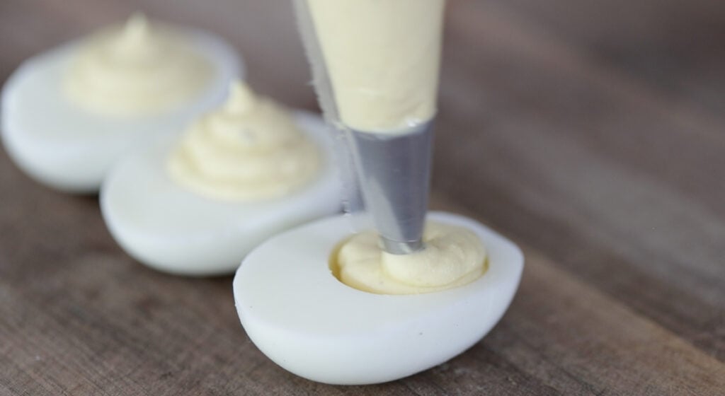 piping deviled egg filling into hard boiled egg halves