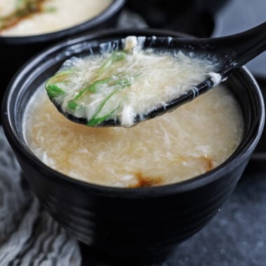 a spoonfull of egg drop soup over a bowl