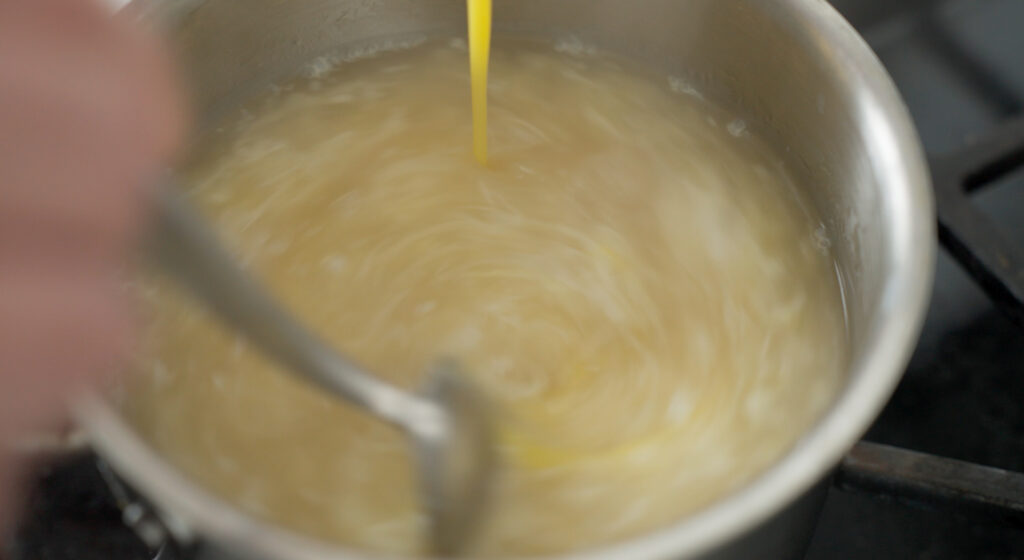 Spoon stirring while eggs are being poured into the pot