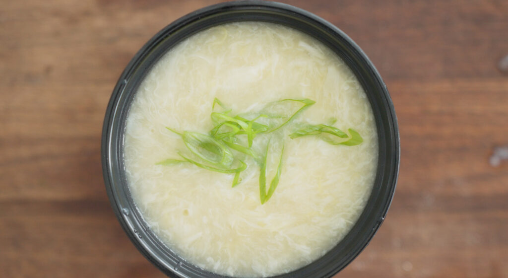 Finished egg drop soup in a black bowl with green onions on top