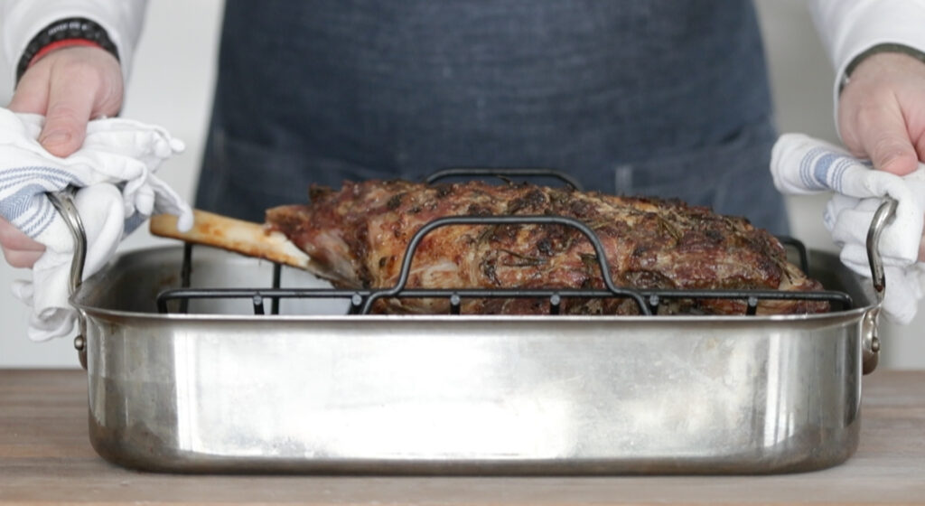 a roasted bone in leg of lamb in a roasting pan with a rack