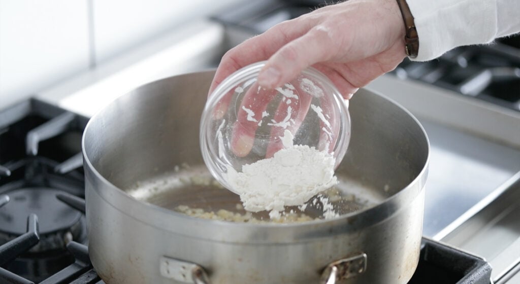 adding flour to the pot with onions and garlic