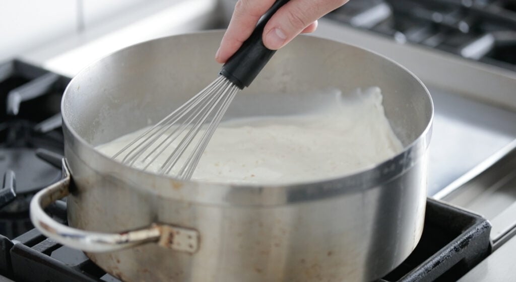 mixing a creamy sauce in a large rondeau pot