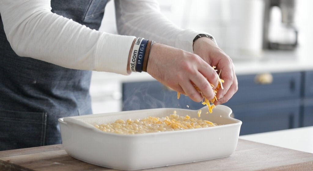 sprinkling cheese on top of macaroni and cheese in a casserole dish