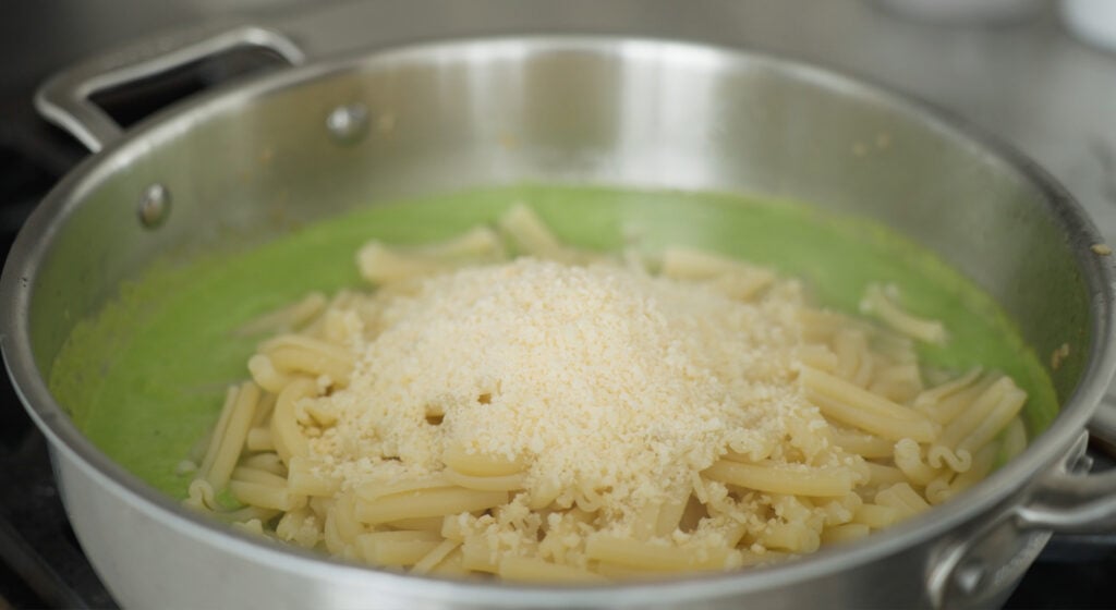 Pasta and cheese added to the pot on top of the green sauce