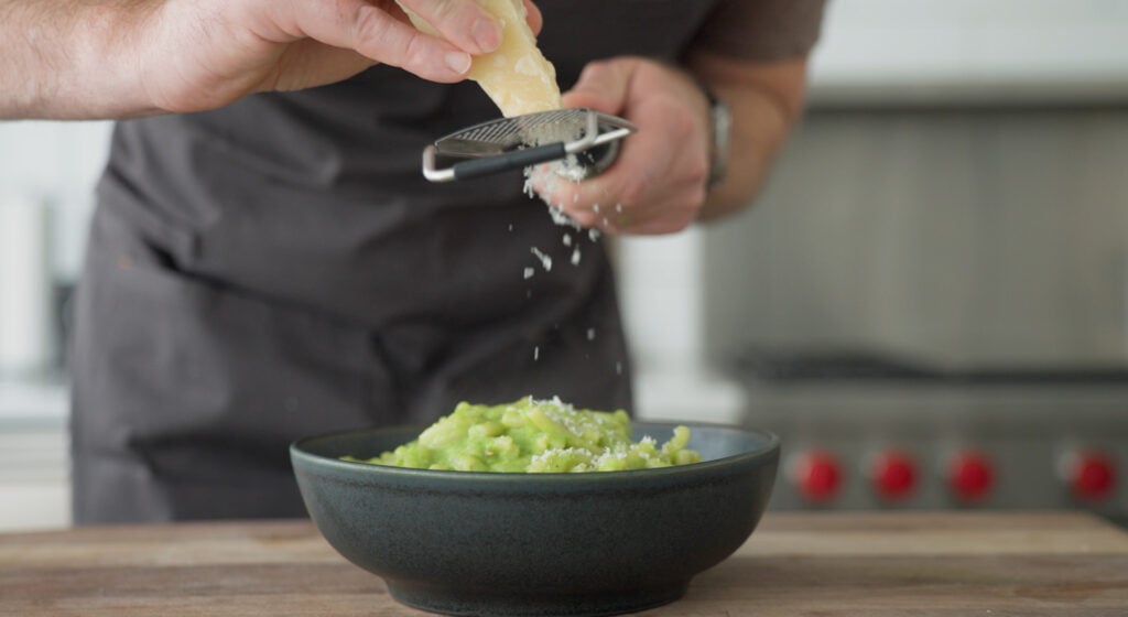 Pasta with peas in a serving dish being topped with freshly grated cheese