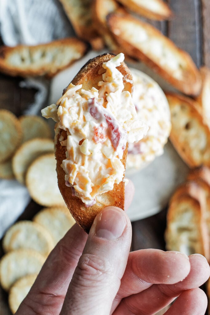Hand holding a piece of bread with pimento cheese dip spread on it