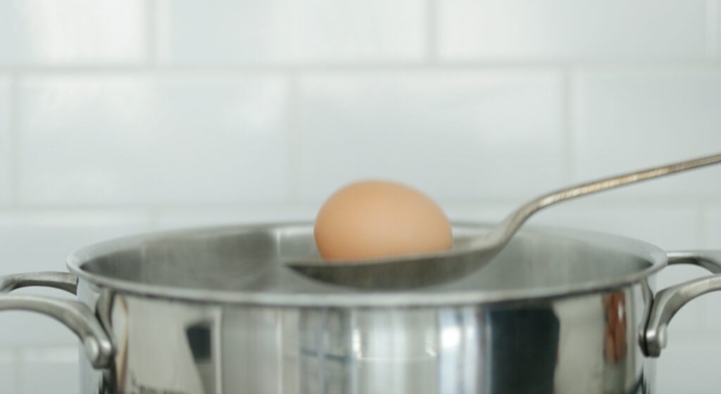 adding an egg on a spoon to a pot of boiling water