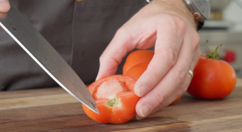 Using a knife to remove the stem from a tomato half