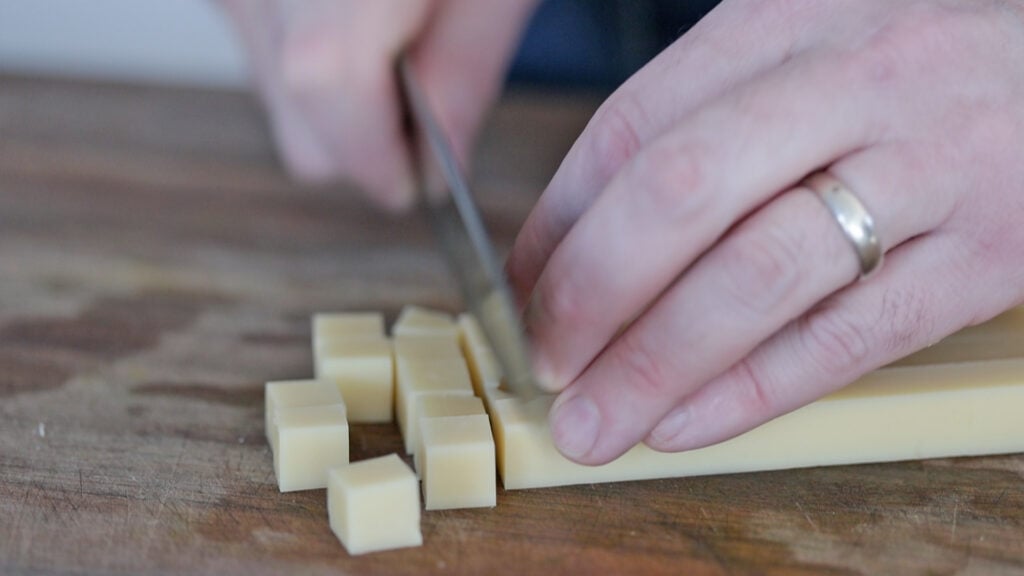 slicing chunks of swiss cheese on a cutting board