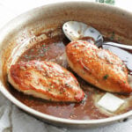 cooked chicken breasts in a pan with sauce and a spoon