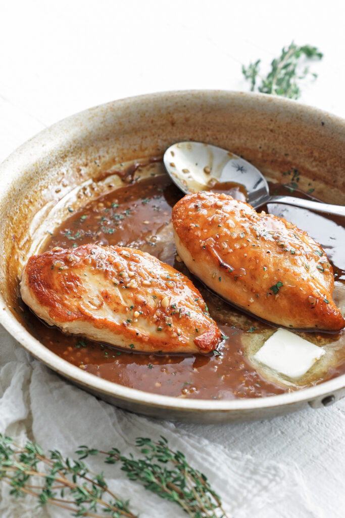 cooked chicken breasts in a pan with sauce and a spoon
