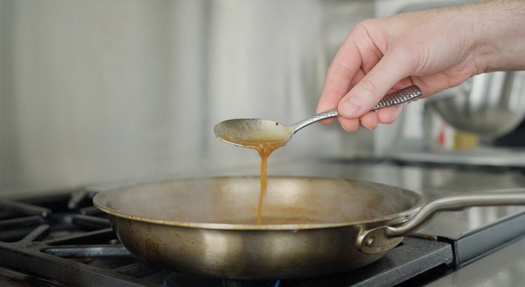 A spoon tilted as the pan sauce pours over the edge