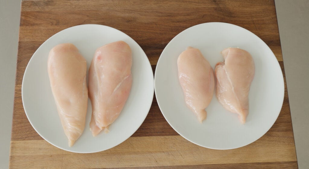Two white plates each with 2 boneless, skinless chicken breasts