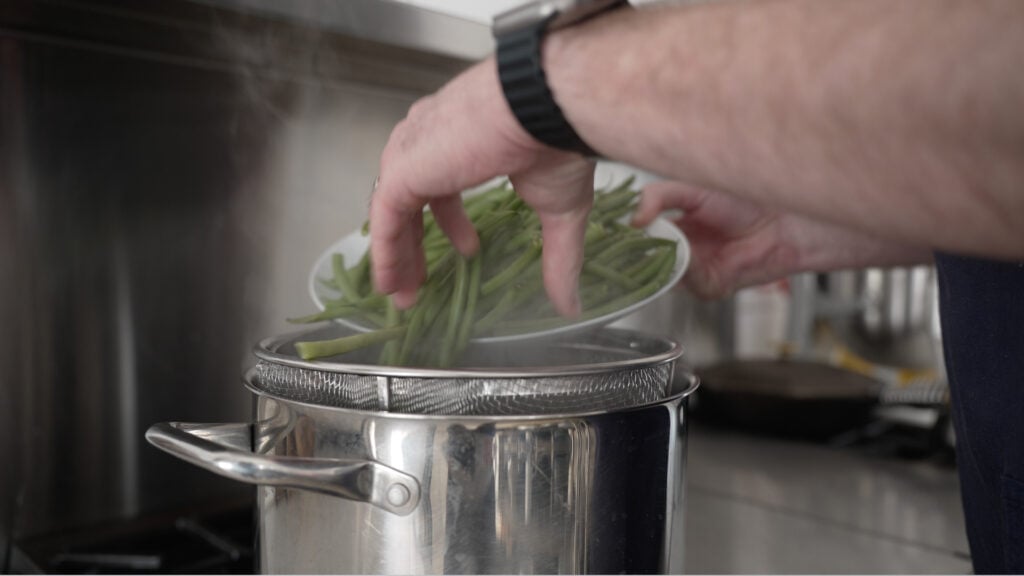 Adding green beans to a steamer basket in a pot of boiling water