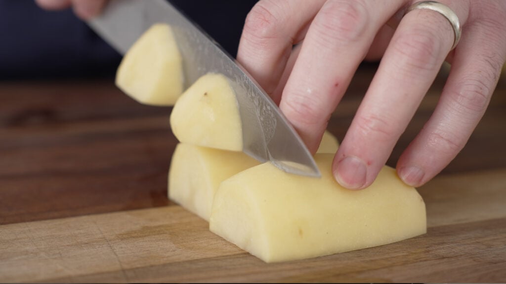 Cutting peeled potatoes into large chunks on a cutting board