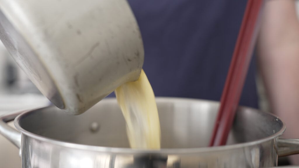 Pouring the hot cream and butter mixture into the pot with potatoes