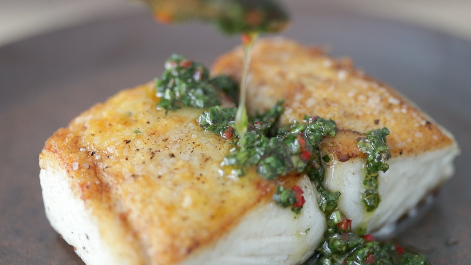 adding chimichurri sauce to cooked halibut