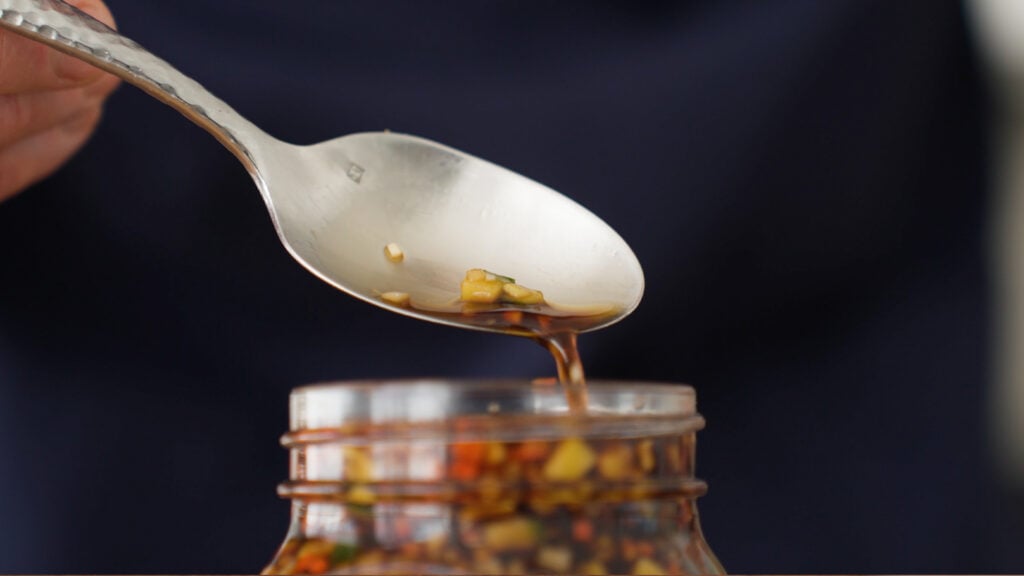 Close up of sauce dripping off of a spoon into the jar of inasal sauce