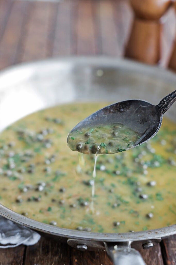 Lemon caper butter sauce dripping off of a tilted spoon