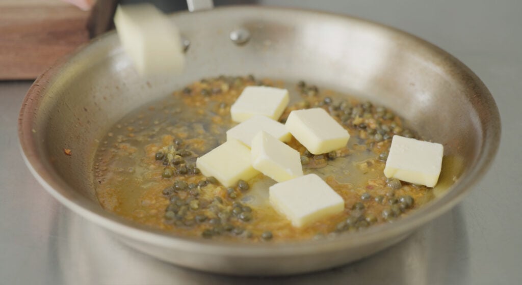 Several pats of butter in a pan with the rest of the sauce ingredients