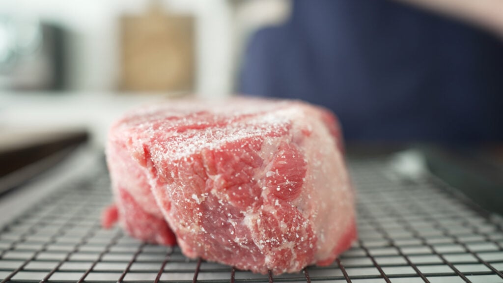 Uncooked roast sprinkled with salt on a rack over a sheet tray