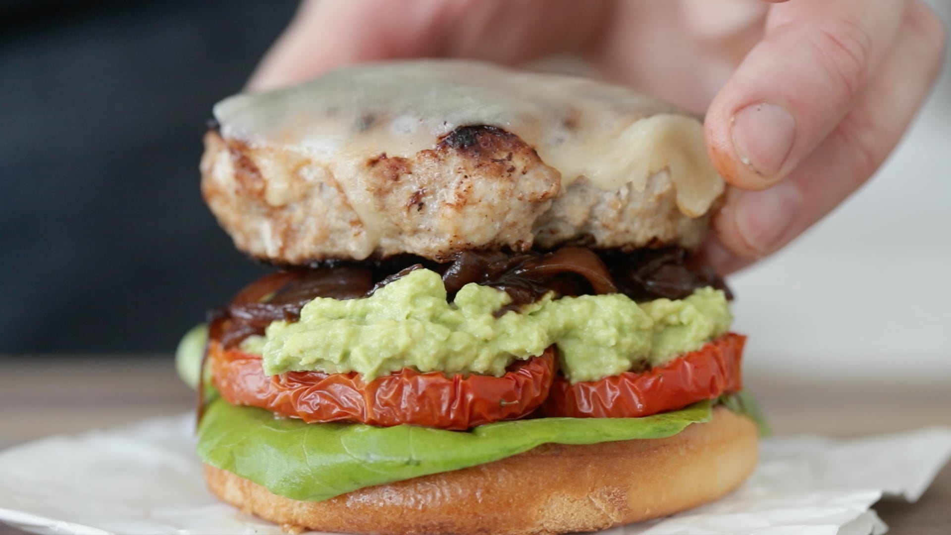adding a turkey burger to a bun with lettuce, tomato, and onion