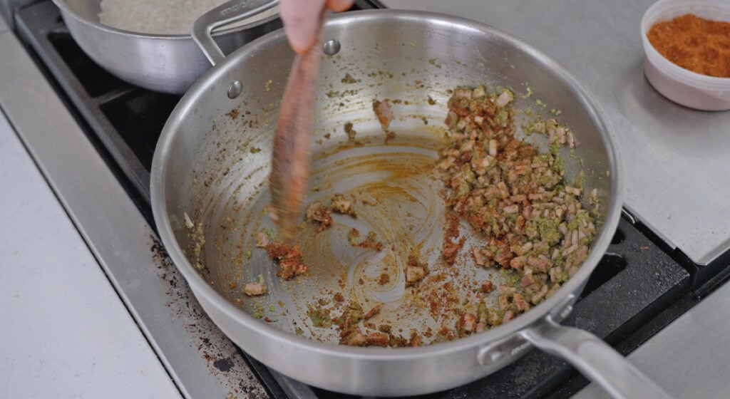 seasoning being mixed into pot with sofrito and ham