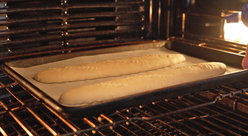 two baguettes on a sheet tray lined with parchment paper in an oven