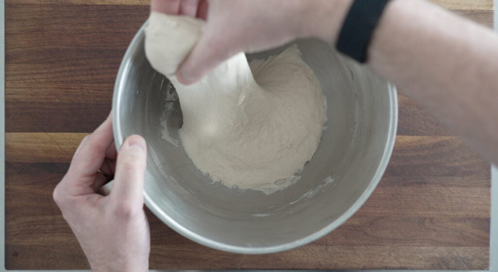 Using hands to stretch the dough in the bowl