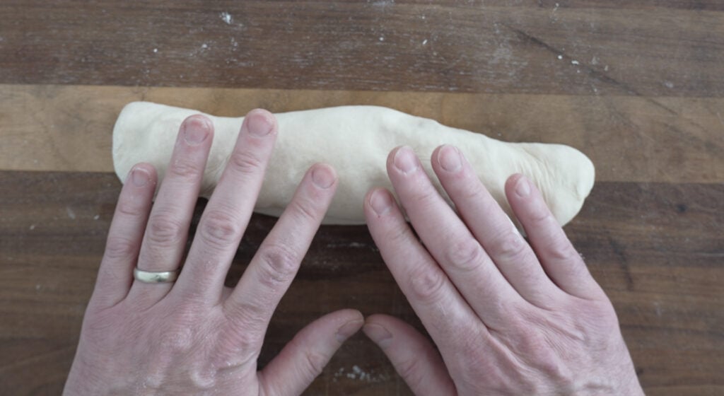 rolling a piece of dough into a baguette shape